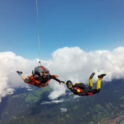 Portrait of tandem skydivers holding hands with female skydiver above clouds and landscape